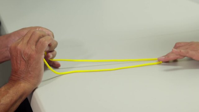 Extreme close-up of an elderly patient practicing occupational therapy by tying knots with a yellow string to restore hand mobility and improve fine motor skills.