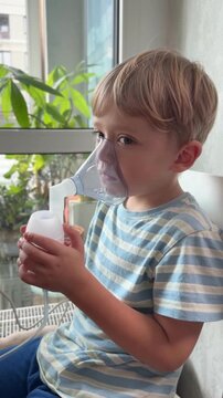 A young boy sits using a nebulizer mask for breathing treatment at home. Pediatric respiratory care, asthma, illness, recovery, medical treatment, health, family care.