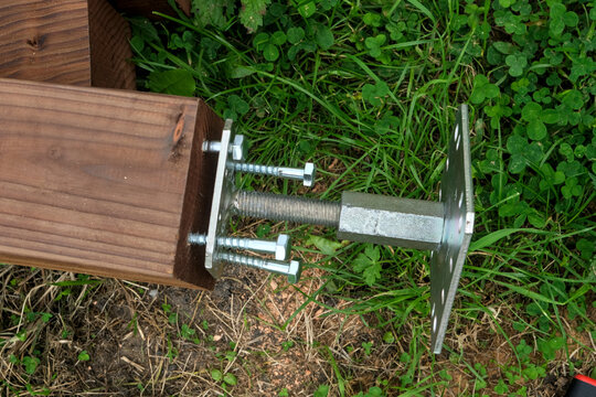 Installation of a galvanized steel base plate for a pergola on a treated wooden post, using lag screws.