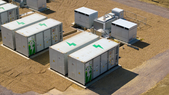 Aerial view of Battery Energy Storage Systems featuring white industrial containers with green lightning bolt logos on a gravel site in Eaton Socon, England, United Kingdom.