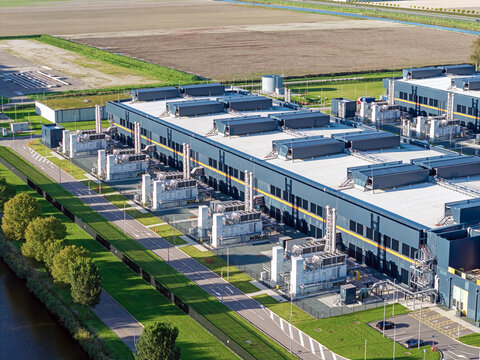Aerial view of the Microsoft datacenter featuring large industrial buildings with cooling units and surrounding green fields in Middenmeer, Noord-Holland, Netherlands.