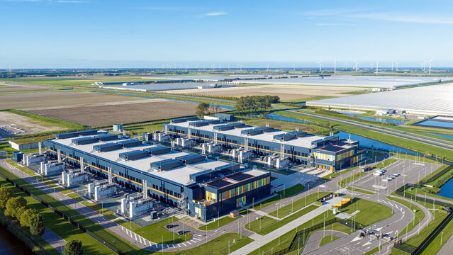 Aerial view of the Microsoft datacenter featuring large industrial buildings surrounded by green fields and greenhouses in Middenmeer, Noord-Holland, Netherlands.