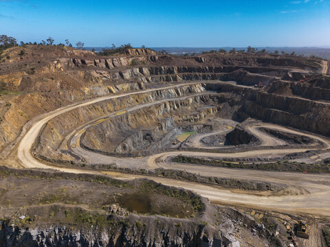 Aerial view of Boral Quarries featuring terraced rock faces, winding dirt access roads, and heavy machinery under a clear blue sky Melbourne, VIC, Australia.