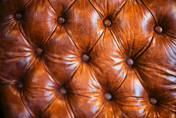 Fototapeta premium Close view of rich brown leather upholstery with deep tufted diamond pattern, round buttons, glossy creases, and handcrafted padded surface detail in interior furnishing