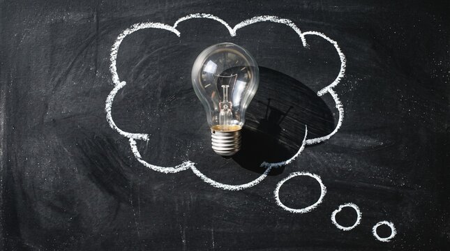 Clear lightbulb placed inside a hand drawn chalk thought bubble on a black chalkboard surface with innovation