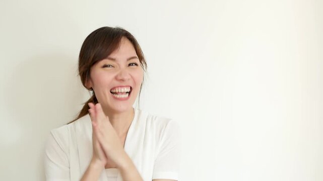 30s adult southeast asian woman laughing joyfully while clapping hands and doing a fist pump gesture, celebrating success