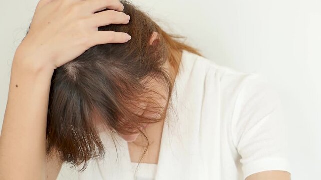 asian woman in her 30s suffering from headache and migraine indoors, touching head with tired and painful expression, closeup shot