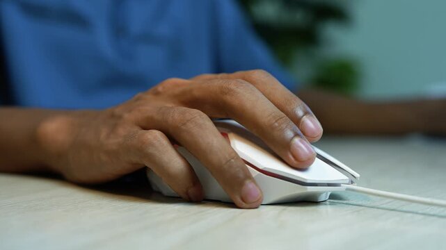 Hand using wired computer mouse at desk, Close-up of a person's hand using a wired computer mouse on a desk, showing everyday technology, online work, and digital navigation.