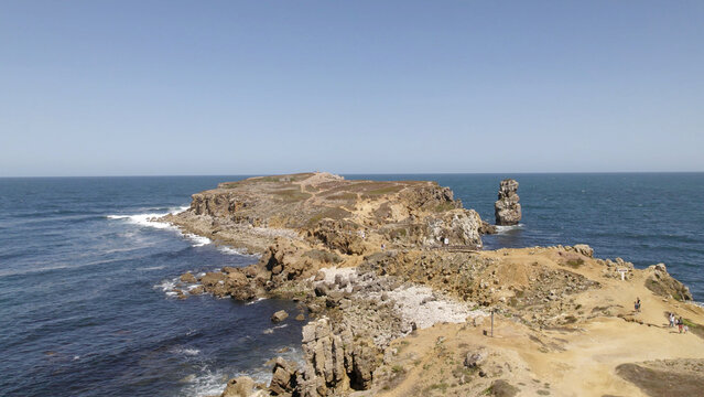 Aerial view of the rocky coastline and cliffs of Peniche, featuring rugged terrain, crashing waves, and a prominent sea stack in the Atlantic Ocean, Peniche, Leiria District, Portugal.