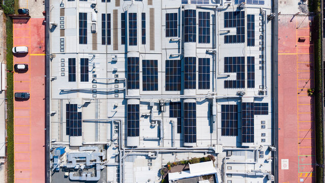 Aerial view of a supplement factory featuring extensive rooftop solar panels, industrial ventilation systems, and surrounding parking areas in Milan, Lombardy, Italy.