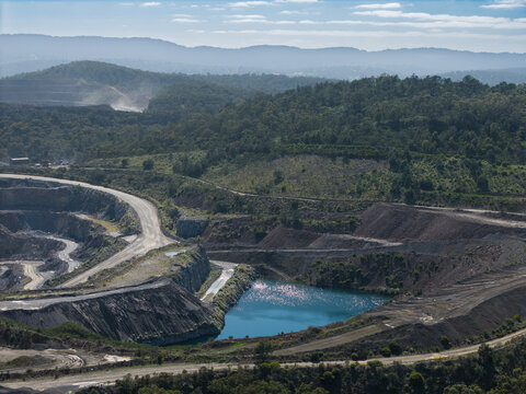 Aerial view of Boral Quarries featuring deep excavation pits, a vibrant blue water reservoir, and surrounding forested hills in Lysterfield, Victoria, Australia.