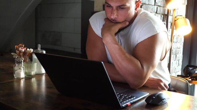 Focused Young Athletic Man Working on Laptop Computer at Cozy Cafe Table Remote Work Freelance Digital Nomad Concept