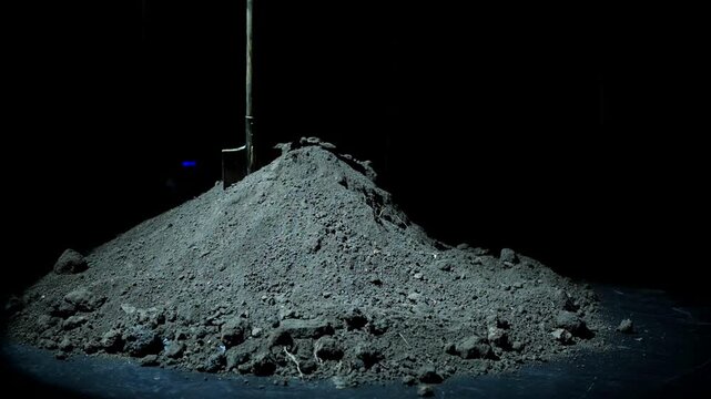 A digging shovel remains stuck in a huge mound of earth that looks like a grave in the middle of a dark night. The empty surroundings intensify the feeling of mystery, fear, and suspense.
