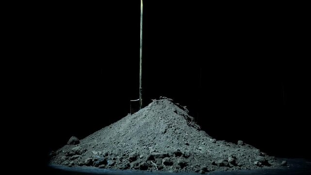 A shovel stands embedded in a large mound of soil resembling a grave in the darkness of night. The eerie scene is surrounded by deep shadows and an ominous atmosphere.