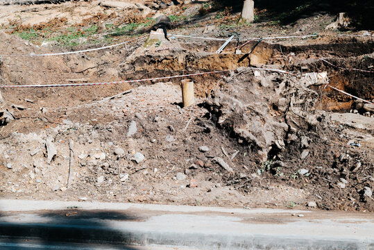 Excavated earth and debris are visible at a construction site, with safety barriers and caution tape marking the area. The ground shows signs of recent digging and soil displacement