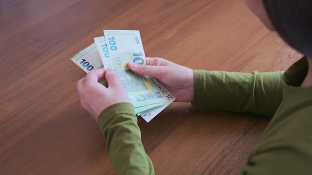 person calculating euro cash bills on wooden tabletop with focused attention displaying paper currency valuation financial stability banking transactions and income distribution inside