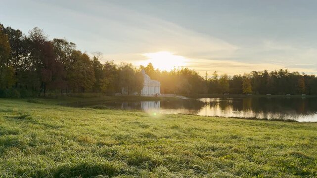 Tracking shot of the Grotto pavilion glowing by a peaceful pond in Catherine Park, Pushkin, Saint Petersburg. Warm sunlight shines through trees, creating a serene, magical atmosphere.