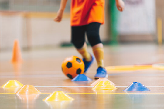 Junior Player Dribbling Orange Soccer Ball Through Cones During Indoor Futsal Skill Drill - Youth Sports Training Session