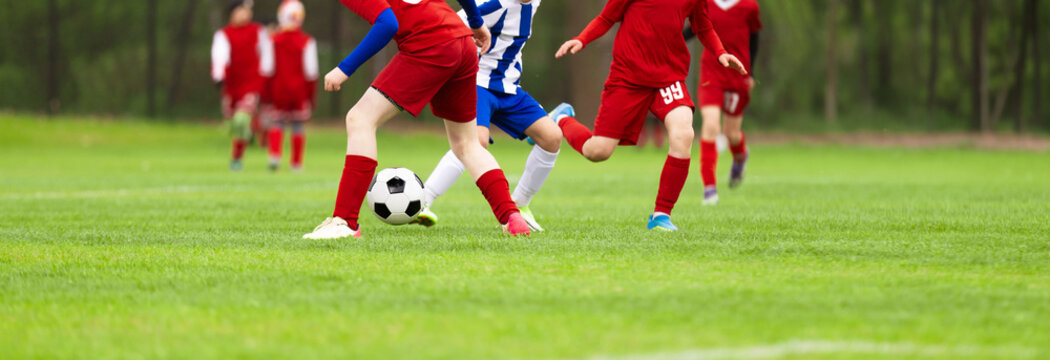 Junior Soccer Players in Red Uniforms Dribbling and Challenging for Ball Possession on Outdoor Grass Pitch - Youth Football League Match Action