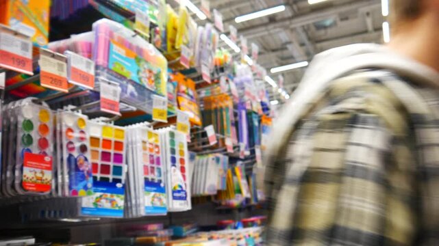 Focused young schoolboy examining a packed set of colorful pens in a creative art supply aisle and walking away. Creative hobby and back-to-school preparation concept