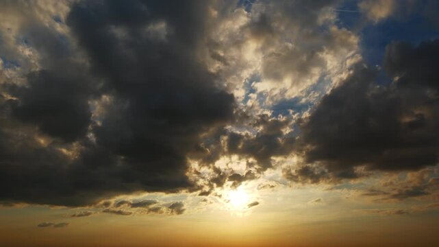 Time lapse of a dramatic sunset with layers of dark and orange clouds moving in the sky and the sun setting behind the horizon