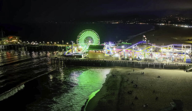 Aerial view of Santa Monica Pier at night with its illuminated ferris wheel and amusement park rides glowing against the dark ocean in Santa Monica, CA, United States.