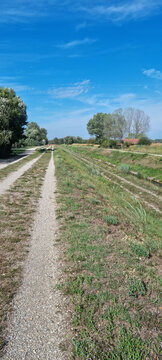 A vertical view of a gravel double track road on a grassy water levee next to Varazdin lake under a vibrant blue sky.