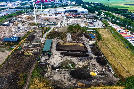 Aerial view of an industrial waste management facility featuring large piles of compost and soil, industrial buildings, a wind turbine, and surrounding green fields in the Netherlands.