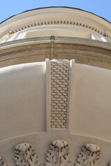 A low angle vertical view of a beige building facade showing a curved balcony underside decorated with a fish scale pattern panel and acanthus leaves. © nahhan