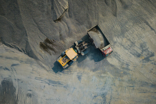 Aerial view of a yellow excavator loading gravel into a dump truck at a quarry site in Yogyakarta, Special Region of Yogyakarta, Indonesia.