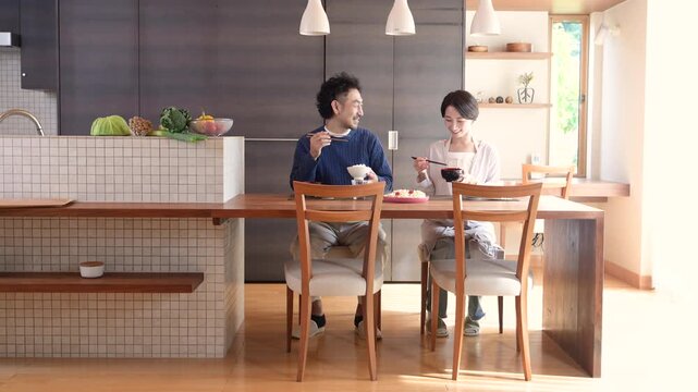 注文自宅のようなインテリアの綺麗な食卓で食事をする日本人夫婦、食事をしながら会話する仲良しの幸せなライフスタイルカップルイメージ全身動画