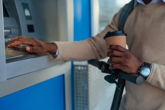 Man using ATM with scooter and coffee