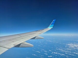 Fototapeta premium Airplane wing flying high in the clear blue sky over clouds during a sunny flight