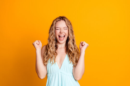 Young woman celebrating with raised fists and joyful expression against a vibrant orange background conveying excitement, confidence and energetic positivity