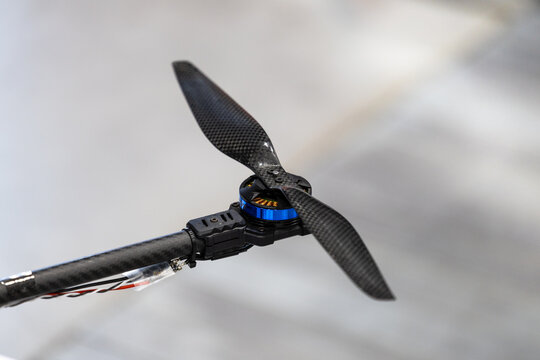Carbon fiber drone propeller mounted on brushless electric motor arm. Close view displays composite rotor blade on unmanned aerial vehicle frame.