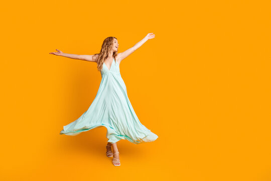 Joyful woman in flowing mint dress dancing with arms outstretched against bright orange background