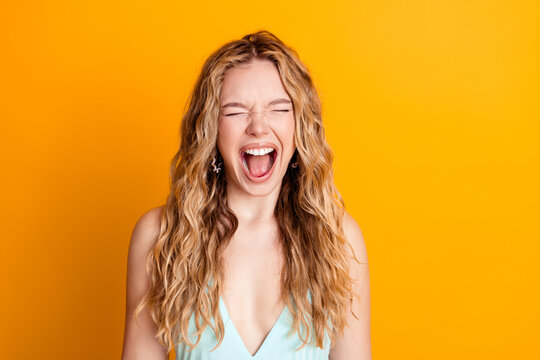 Young woman screaming with joy against a bright yellow background, emotional portrait of excitement and freedom