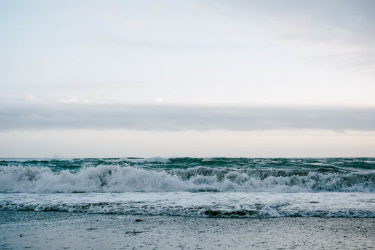 Ocean waves breaking with foam under cloudy sky at shore in Spain