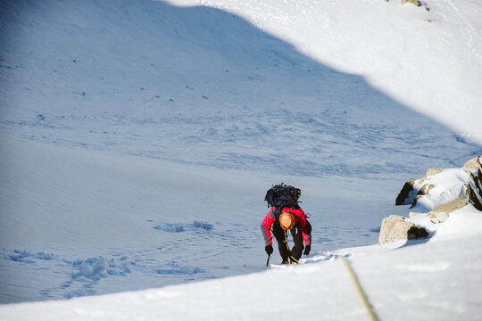 Mountaineer climbing snowy mountain slope with ice axe and rope