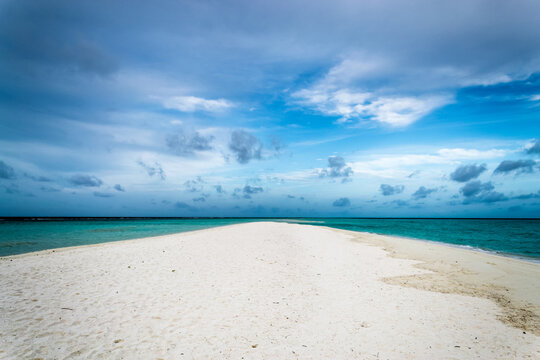Sandbar extending into turquoise ocean under cloudy sky