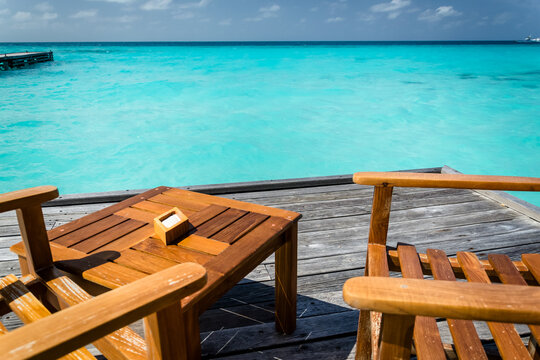 Wooden deck with chairs by turquoise ocean water and pier