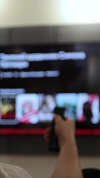 Vertical video. Woman operating a remote control for a smart TV. Channel surfing, focused on the hand and remote control.