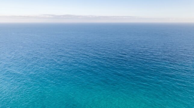 Calm turquoise and deep blue ocean surface stretching to the horizon under a soft pale sky, tranquil seascape with gentle ripples