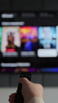 Vertical video. Woman hand operating a remote control for a smart TV. Channel surfing, focused on the hand and remote control.