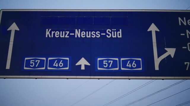 Drive pov under blue direction sign with a white arrow pointing. The sign is on a bridge over a road