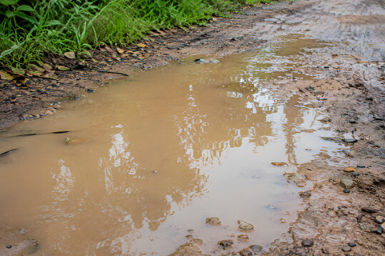 Large muddy puddle on a damaged rural dirt road after rain
