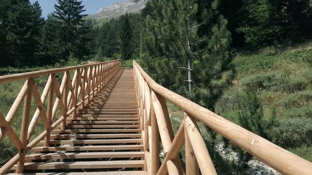Walk pov at wooden staircase with a railing on the side. The railing is made of wood and is on the side of the stairs