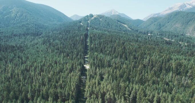 Cable car ski lift wire suspended above a forest with trees, aerial shot