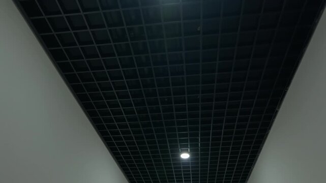 Black grid ceiling with recessed lights in modern building corridor