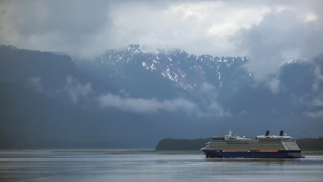 Luxury cruiseship cruise ship liner Solstice sailing the Inside Passage with panoramic mountain range glacier views in Fjord during Alaska Adventure Wilderness cruising with coast line and low clouds